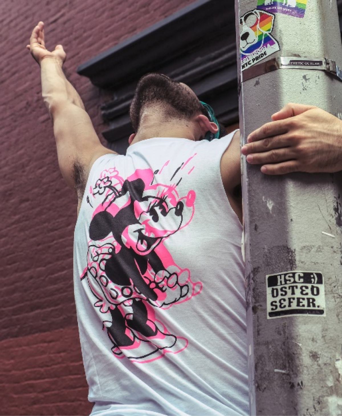 street photography, NY street photography, NY photography, americana photography, urban street life, gay pride, man, minnie mouse shirt, hand raised, hanging off of pole, head up